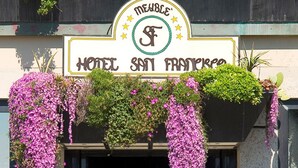 Entrada de hotel con flores moradas colgantes, un cartel que dice 'Hotel San Francisco' y escalones que conducen a la puerta.