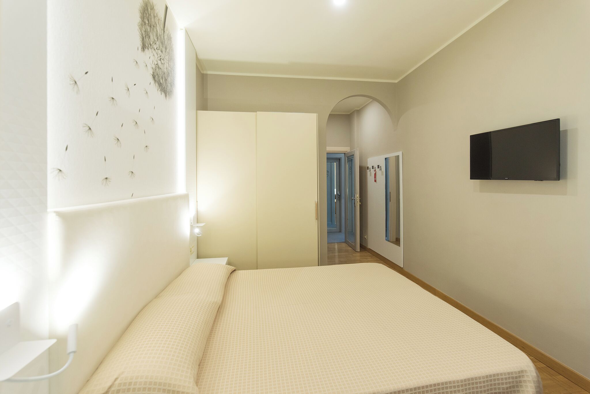 Un dormitorio con cama, televisor, armario y un pasillo que da a otras habitaciones.