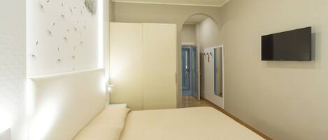 Un dormitorio con cama, televisor, armario y un pasillo que da a otras habitaciones.