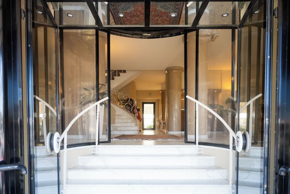 A grand staircase with glass railings leading to a landing, a carpeted area, and a view of a staircase in the background. - San Francisco (Viareggio)