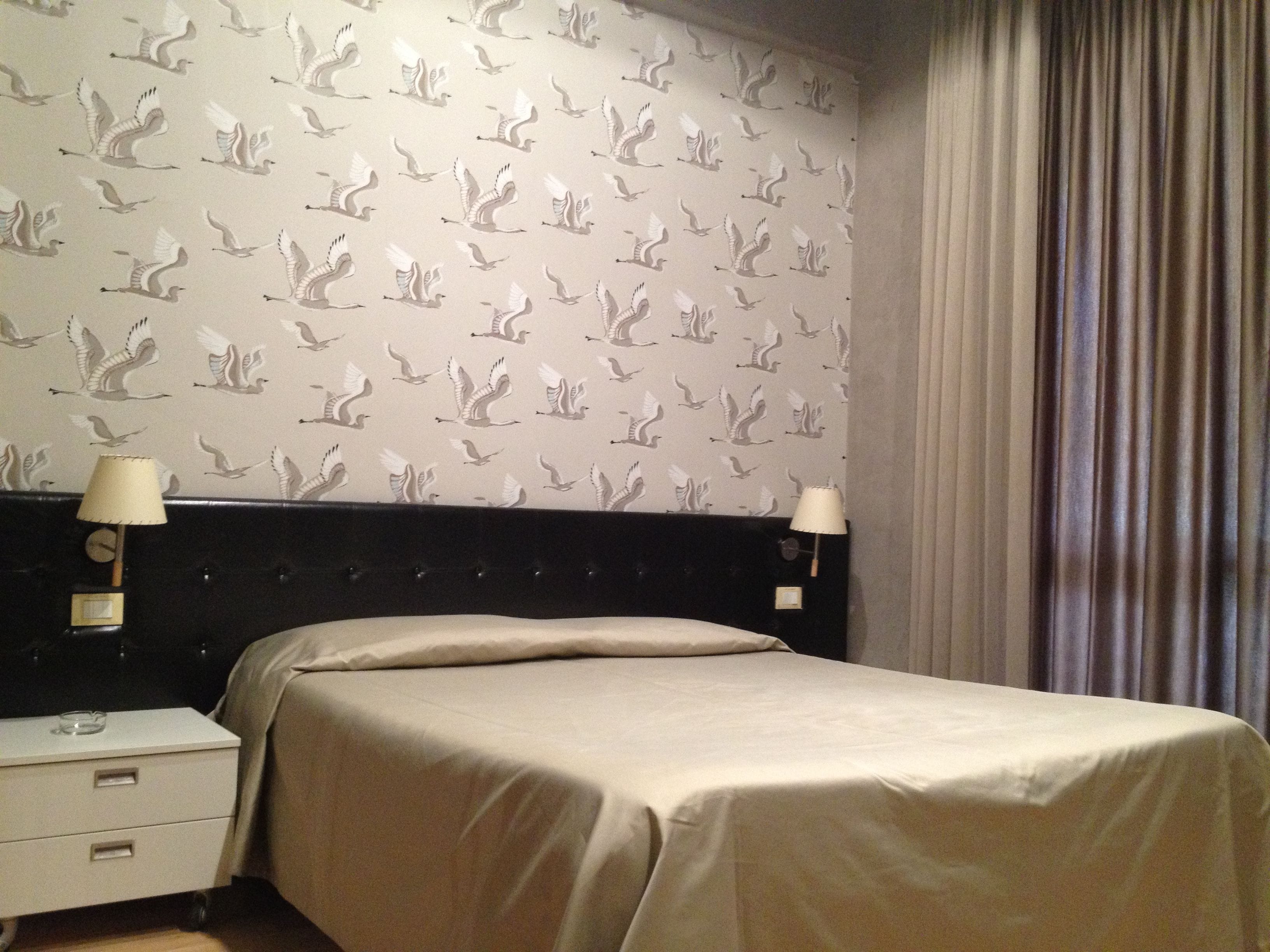 A hotel room with a bed, two bedside lamps, a nightstand, and a curtain.