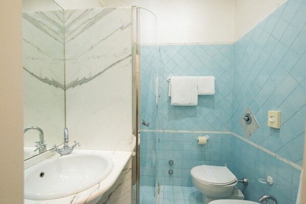 Un baño con lavamanos de mármol, inodoro y ducha con azulejos azules.
