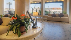 Un lobby espacioso con una mesa redonda de mármol, un sofá y un amplio ventanal con vistas a palmeras y edificios.