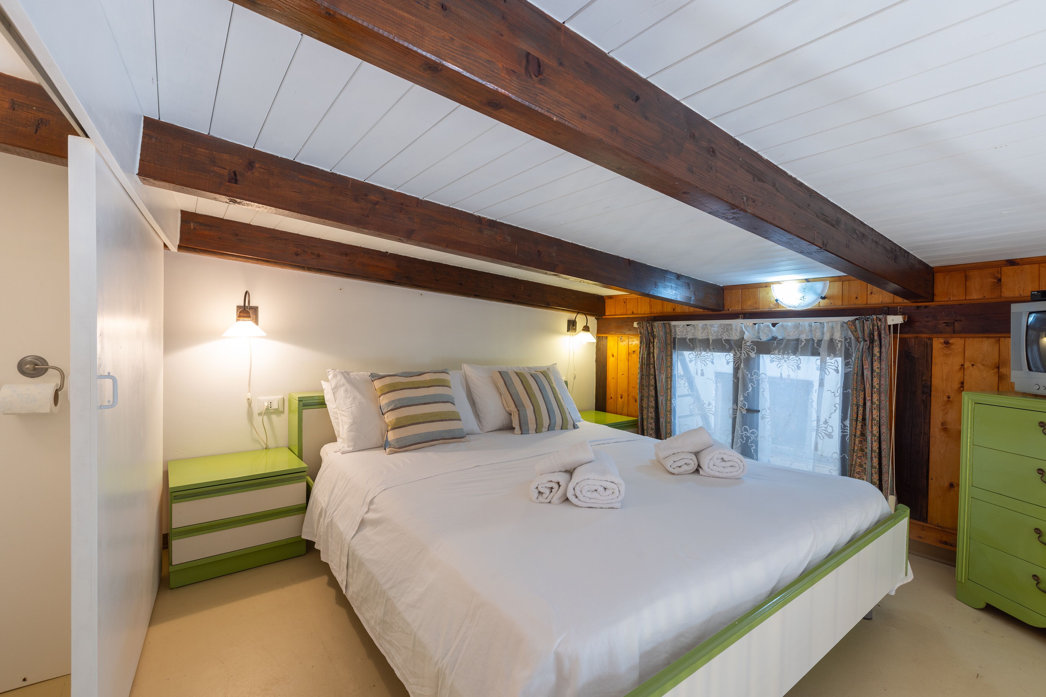 Un dormitorio con cama, mesitas de noche, cómoda y ventana con cortinas.