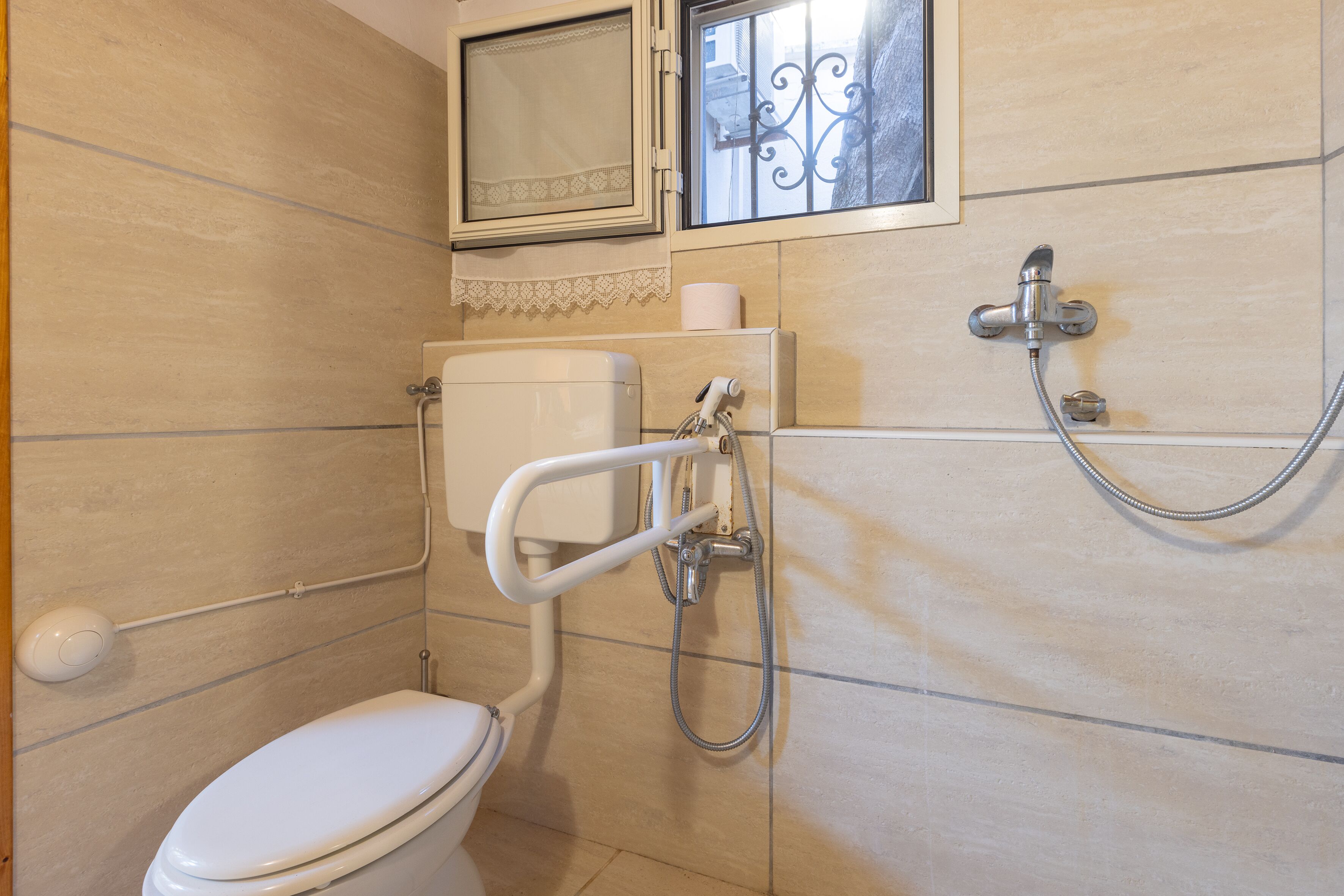 Un baño pequeño con inodoro, ducha y una ventana con herrajes decorativos.
