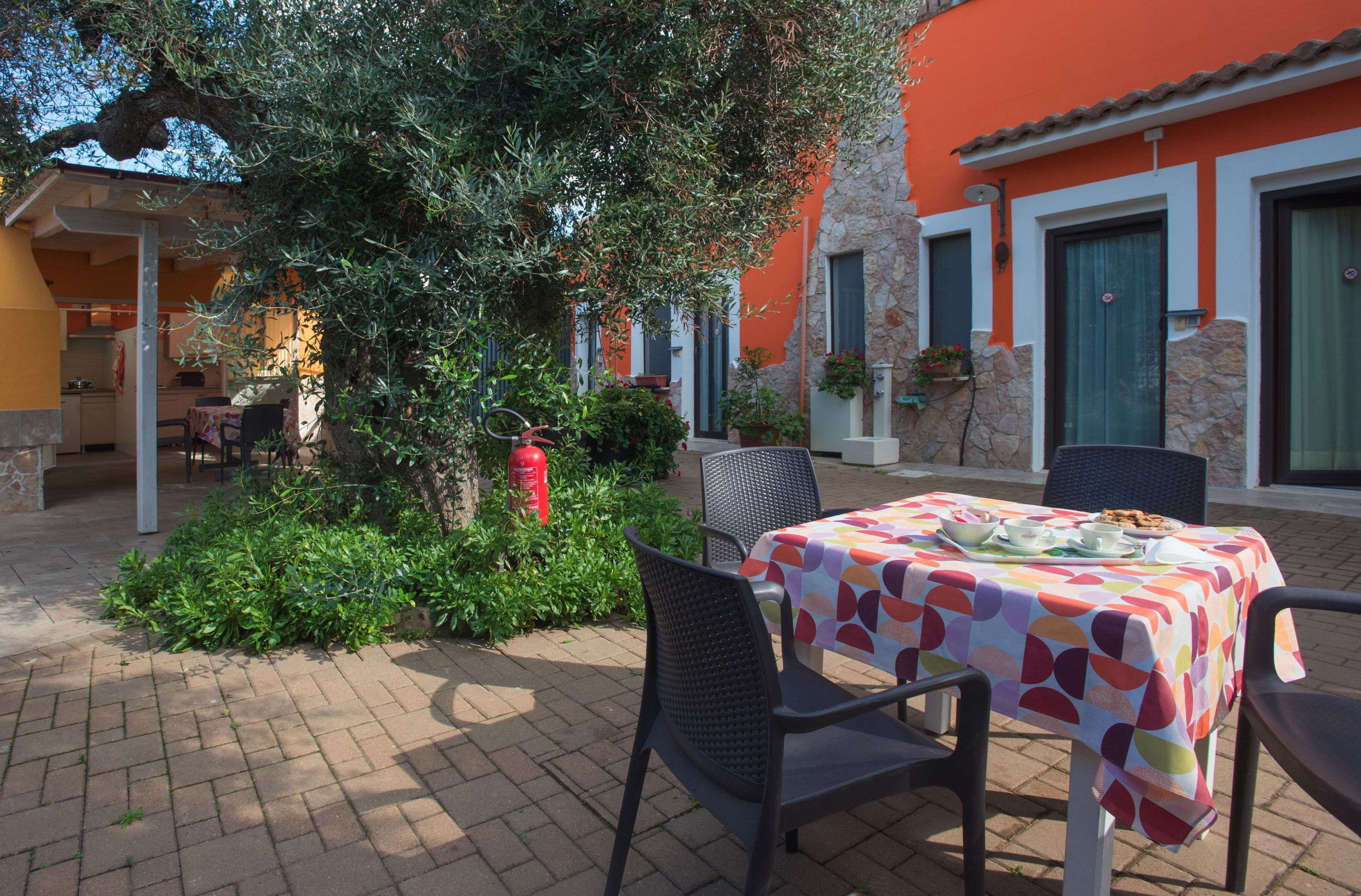 An outdoor dining area with a table covered by a colorful tablecloth, surrounded by chairs.