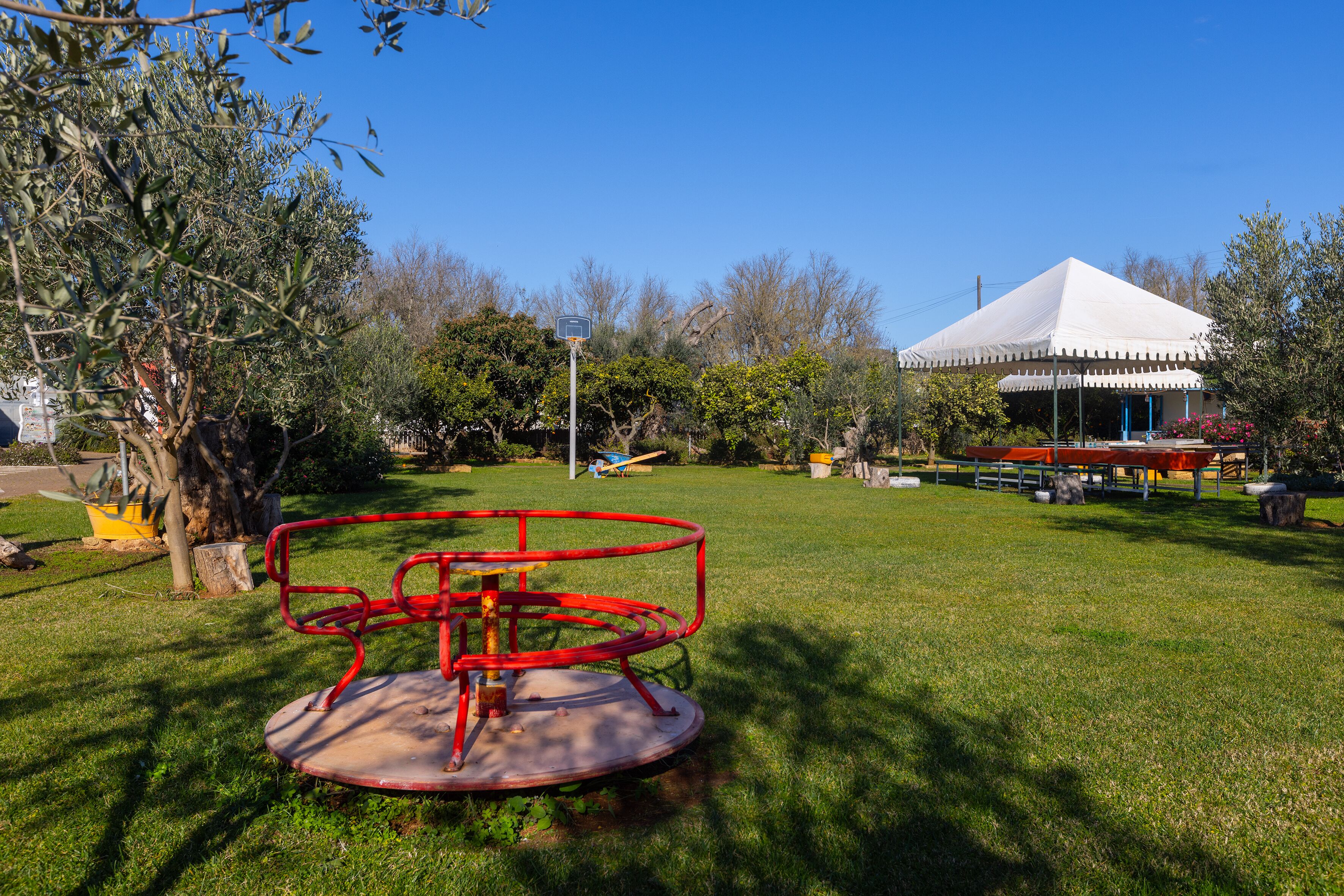 A park with a red merry-go-round, a white tent, and trees.