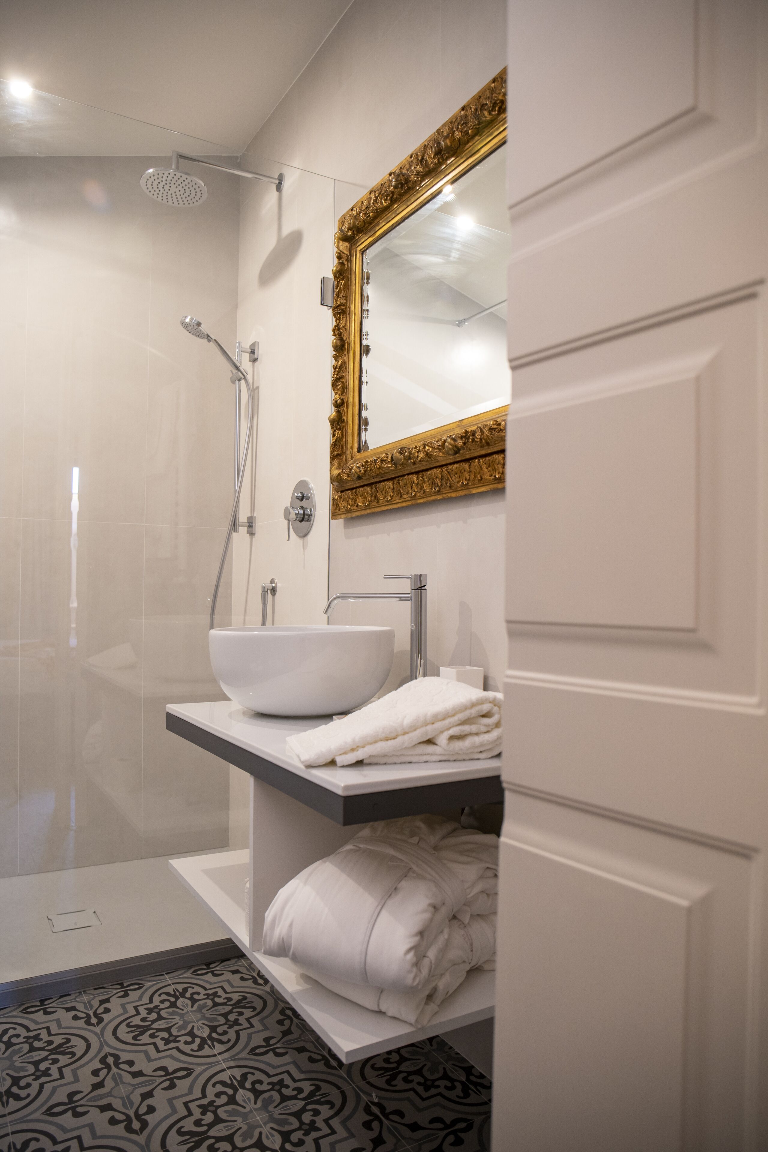 Un baño moderno con un lavamanos blanco, espejo con marco dorado y zona de ducha.