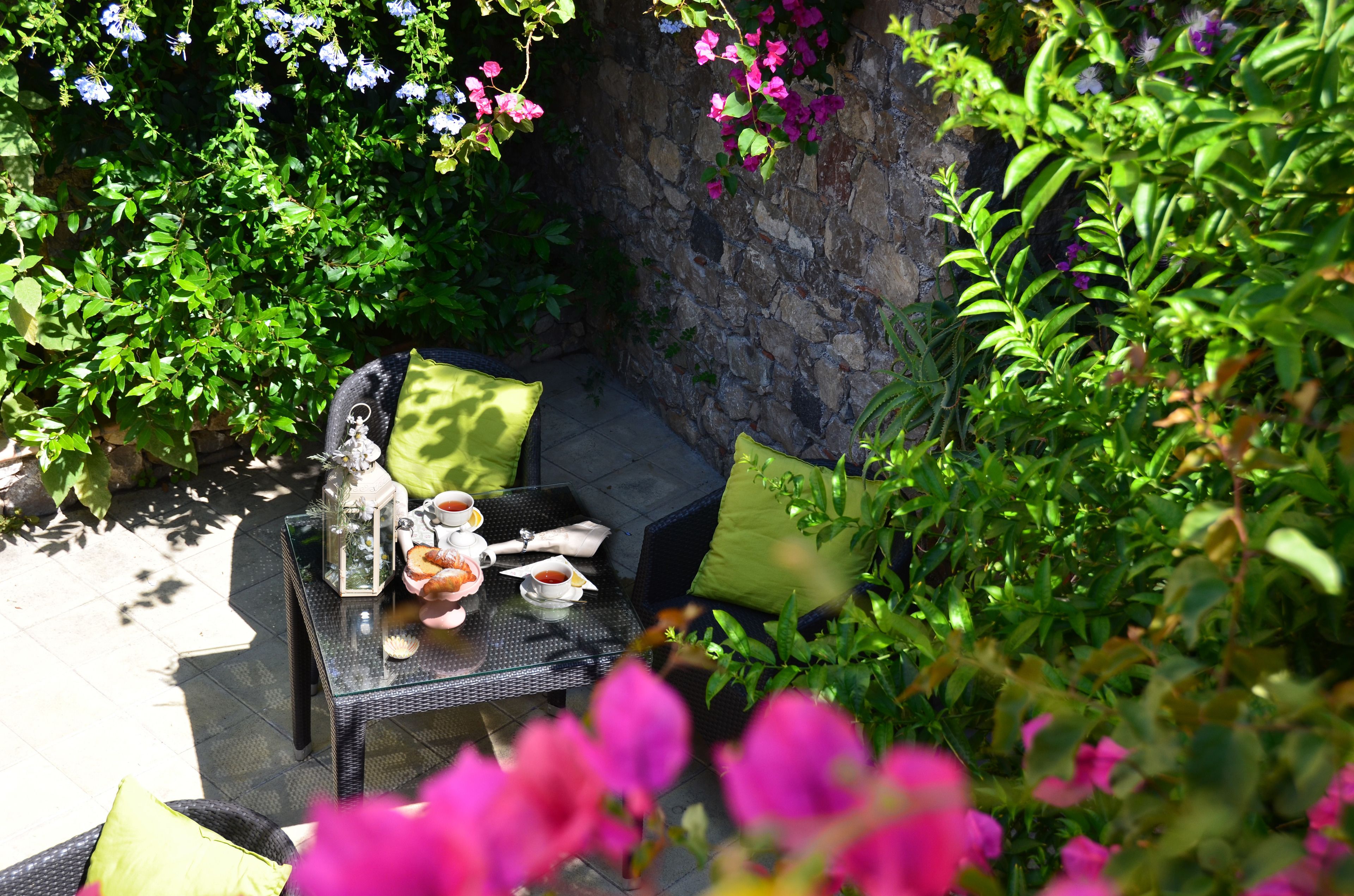 Un espacio de comedor al aire libre con una mesa preparada para dos personas, rodeado de abundante follaje y plantas en flor.