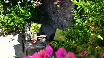 Un espacio de comedor al aire libre con una mesa preparada para dos personas, rodeado de abundante follaje y plantas en flor.