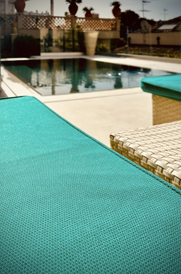 A pool area with a textured blue lounge chair and a wicker chair. - Villa Taormina (Taormina)