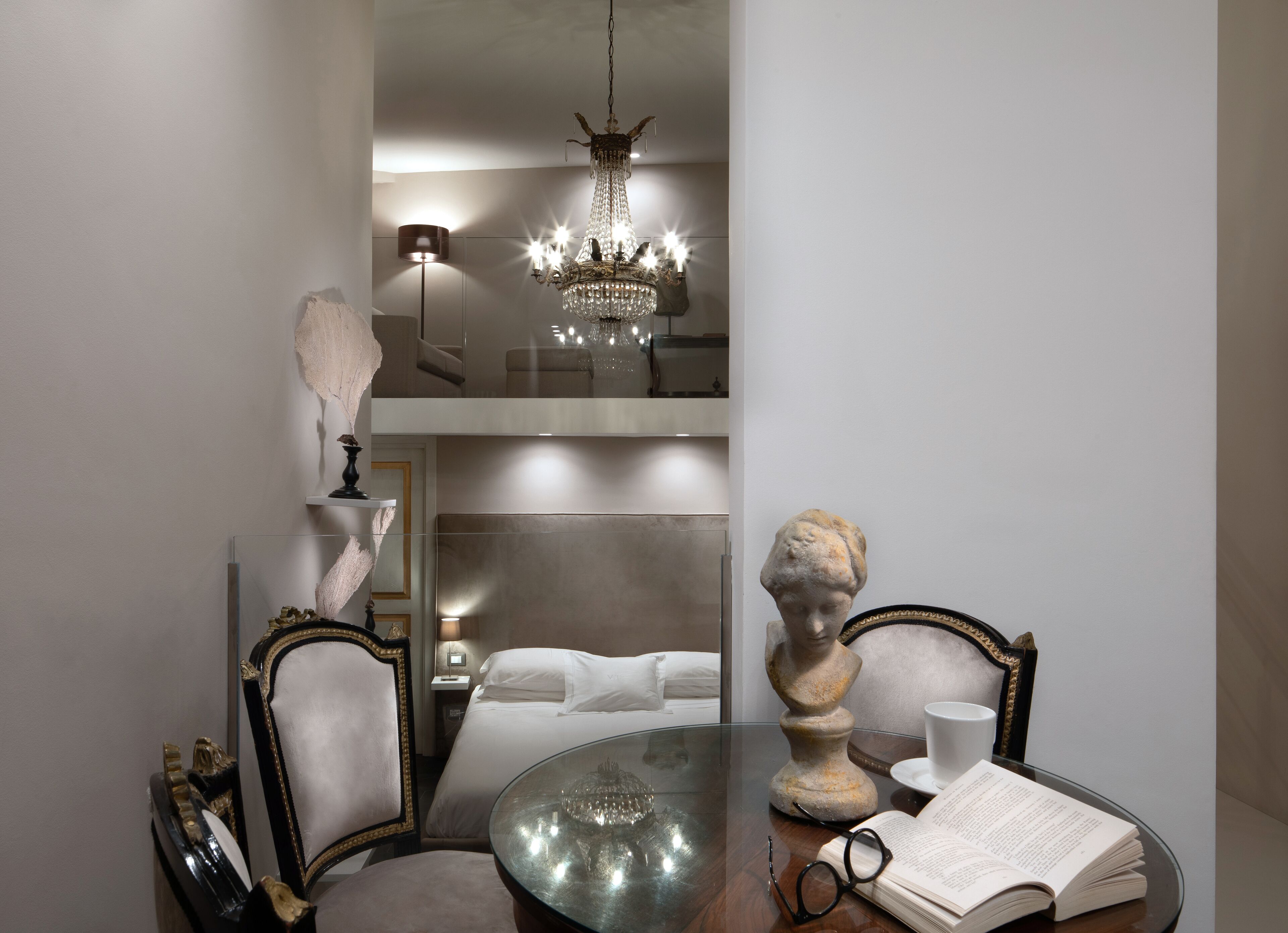 Une pièce avec une table en verre, un livre et une paire de lunettes. Un lustre est suspendu au plafond.