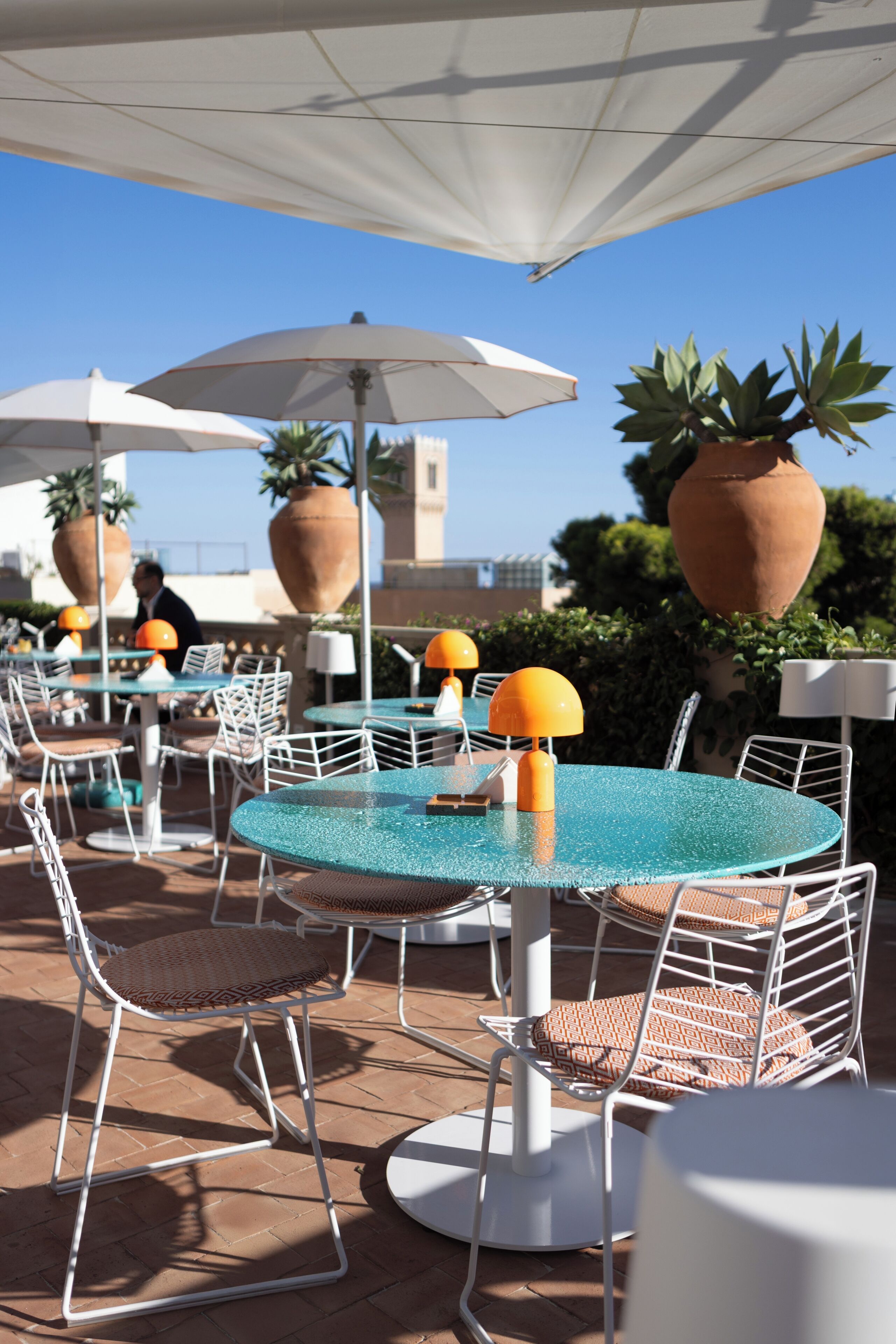 Outdoor seating with round tables and chairs, umbrellas, and potted plants.