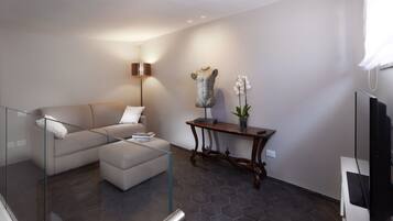 A modern living room with a sectional sofa, a glass coffee table, a floor lamp, a decorative bust, and a potted orchid.