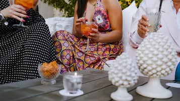Eine Gruppe von Personen sitzt an einem Tisch im Freien, umgeben von Dekoration und einer Kerze, mit Getränken.