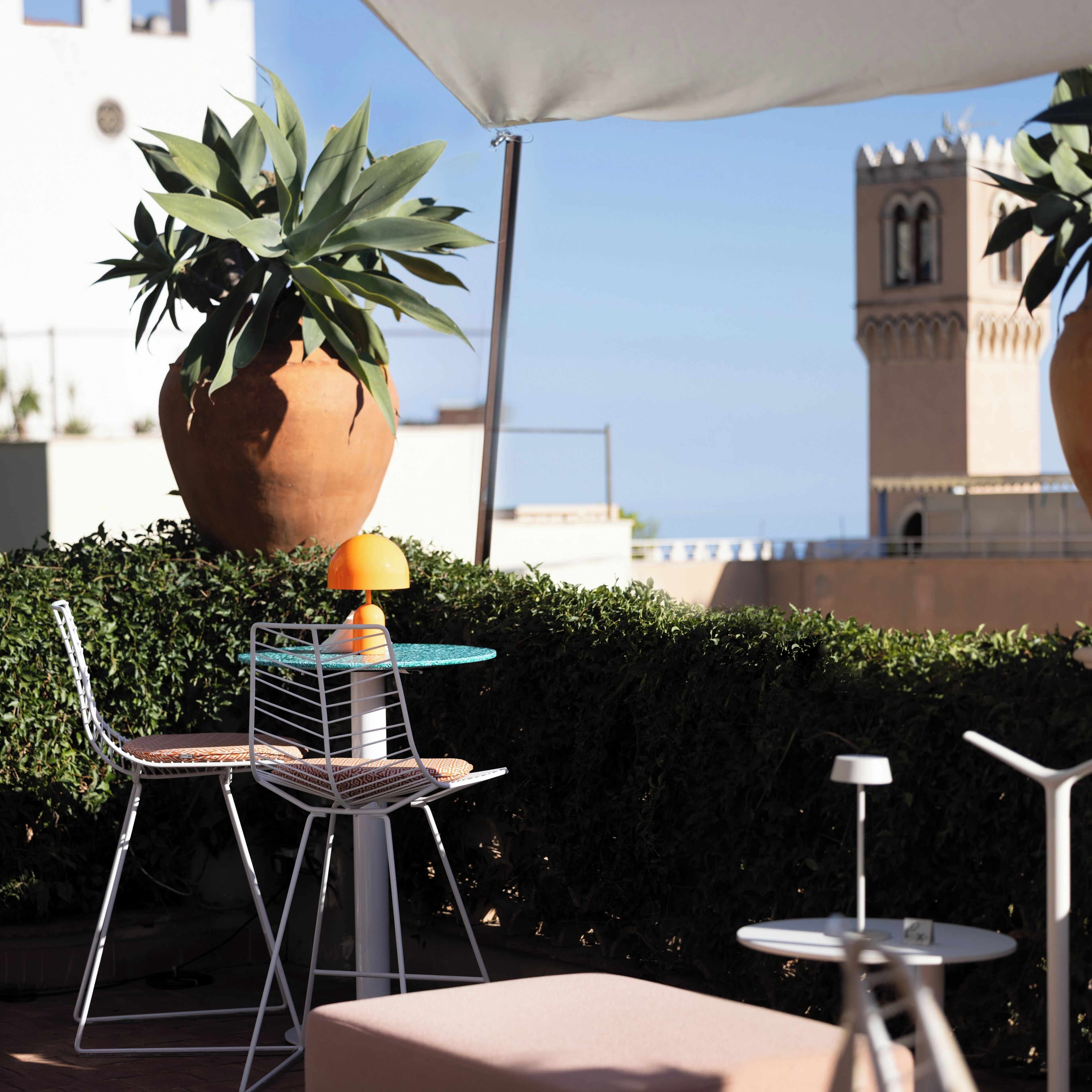 Un área de estar al aire libre con una mesa, sillas, una planta en maceta y vistas a un edificio con una torre.