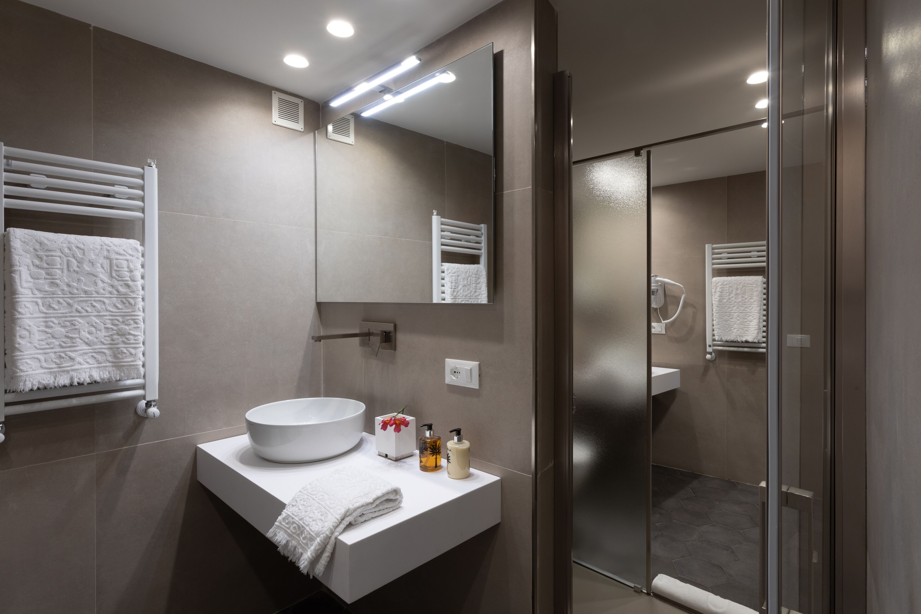 A modern bathroom with a large mirror, a round sink, and a glass shower enclosure.