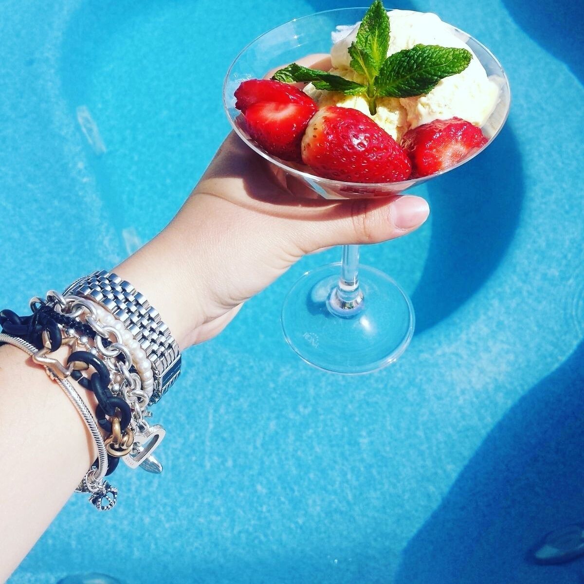 A hand holding a dessert with strawberries and mint, over a blue background.
