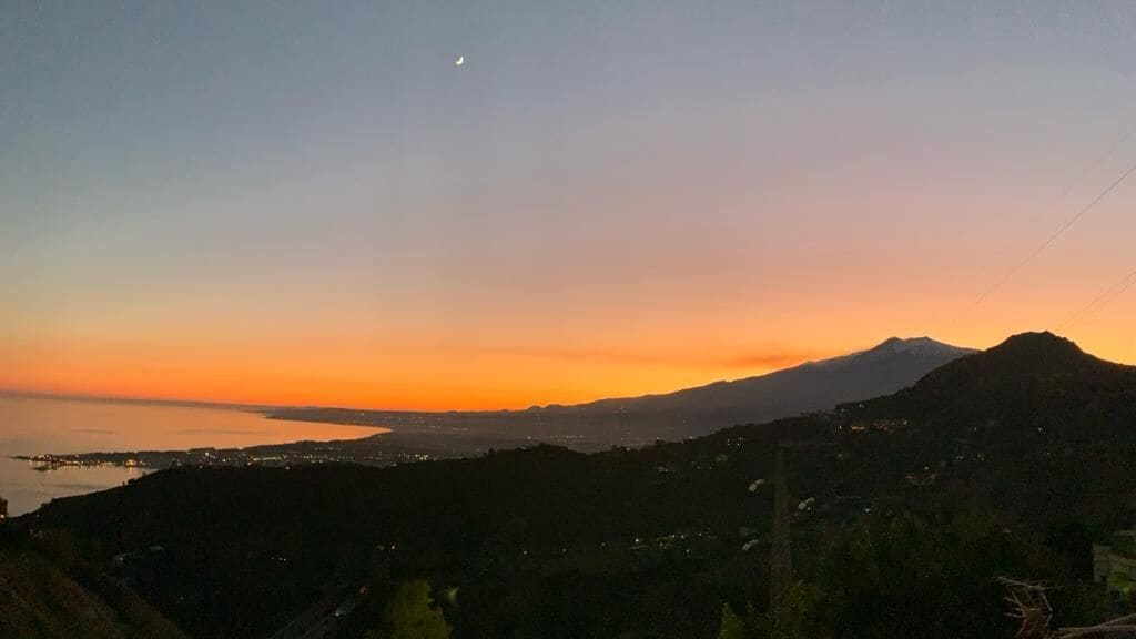 Eine Küstenlandschaft mit einem Berg, einem Halbmond und einem Sonnenuntergang.