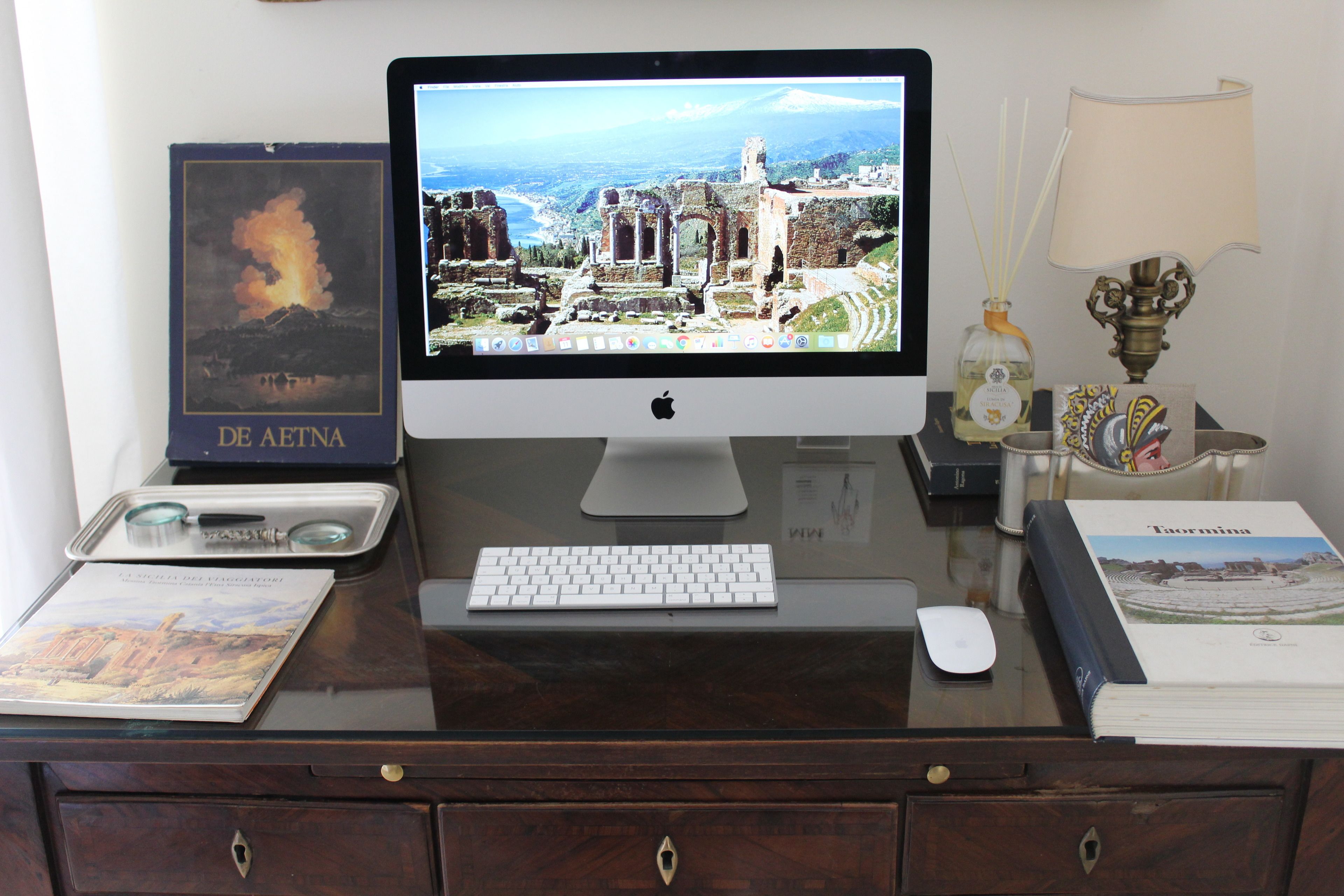 A desk with a desktop computer, a keyboard, a mouse, a lamp, a bottle of reed diffuser, and a book.