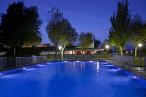 A swimming pool with a surrounding fence, trees, and a building in the background. - Parador de Albacete (Albacete)