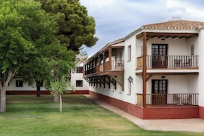 A two-story building with a balcony, a tree in the foreground, and a clear sky. - Parador de Albacete (Albacete)