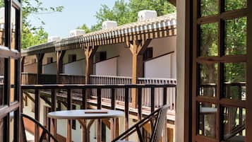 Een balkon met een tafel en stoelen, houten balken en uitzicht op bomen en gebouwen.