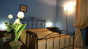 Une chambre à coucher avec un lit en métal, une table de chevet avec une lampe, une plante en pot et un tableau encadré au mur.