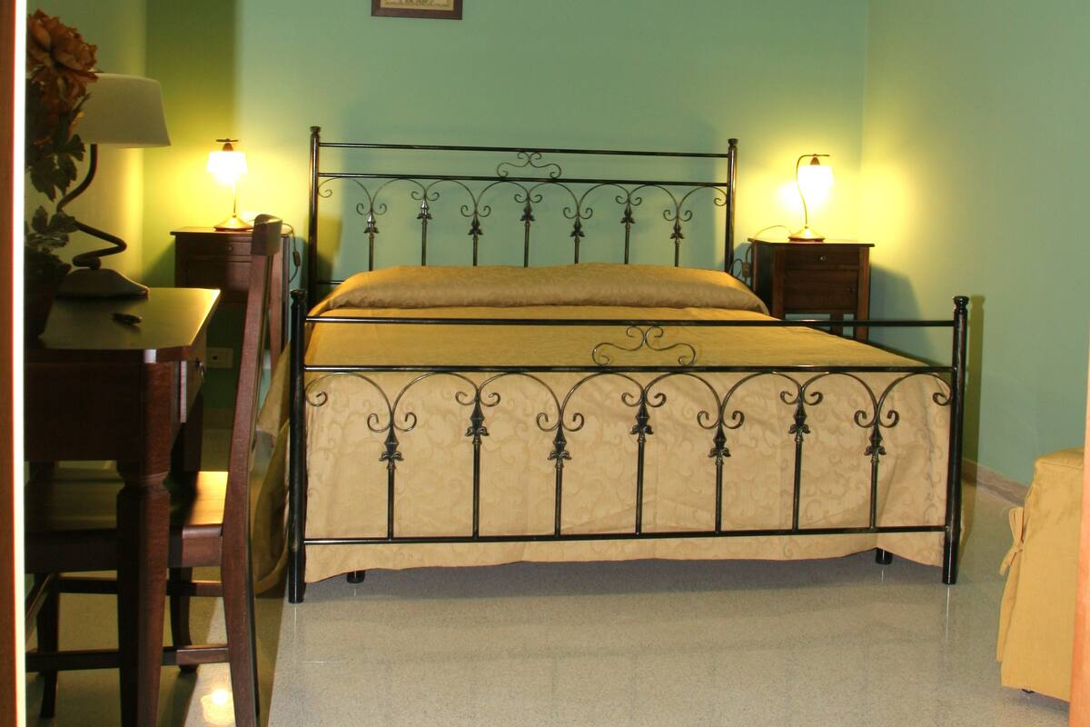 Ein Zimmer mit einem Bett, zwei Nachttischen mit Lampen, einem Sessel und einem kleinen Tisch ebenfalls mit einer Lampe.