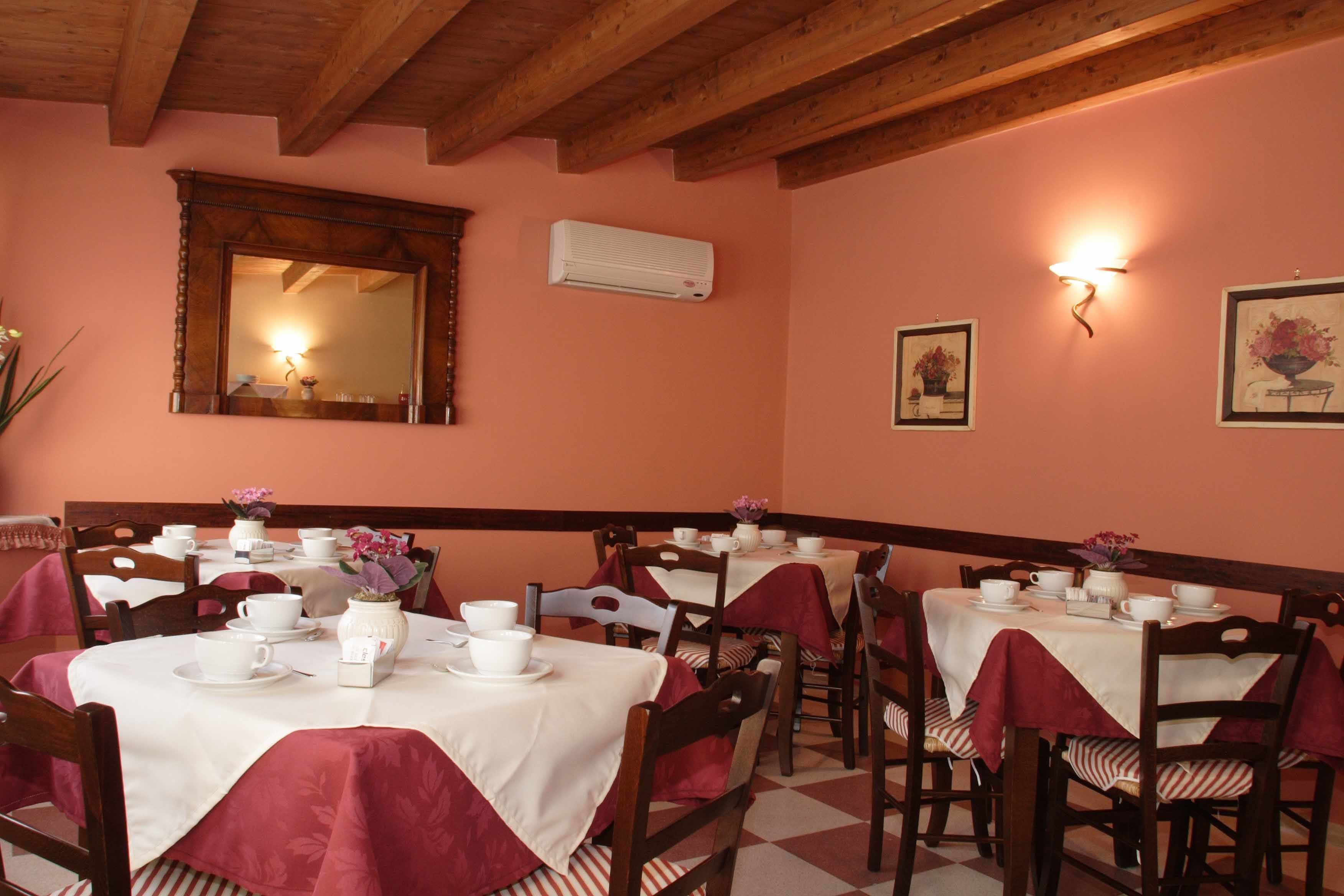 Un espace repas avec plusieurs tables recouvertes de nappes blanches et de serviettes rouges, des chaises en bois et un plafond en bois.
