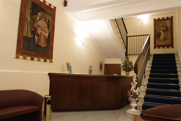 A reception area with a wooden desk, a staircase with blue carpet, and two large framed paintings on the walls.