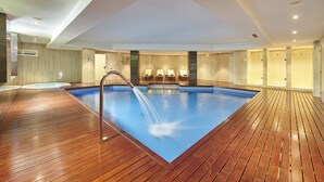 Una amplia piscina interior con cubierta de madera, un elemento decorativo de agua e iluminación empotrada en el techo.