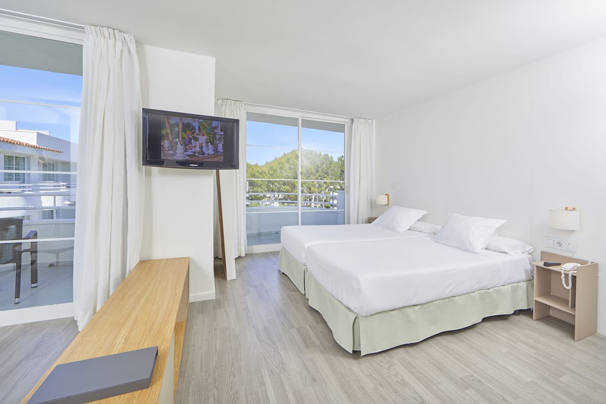 A hotel room with a bed, a TV, a desk, and a balcony with a view of the city.