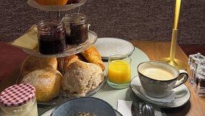 Una mesa con pasteles, frutas y bebidas, frente a una pared de ladrillo con un cuadro enmarcado.