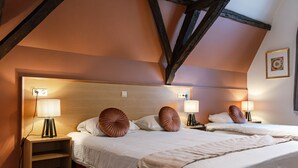Habitación de hotel con cabecera de madera, dos lámparas de noche, mesitas de noche y cama con ropa blanca y almohadones decorativos.