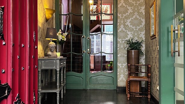 Imponente entrada con puerta verde, un candelabro y una escalera que conduce a un nivel superior.