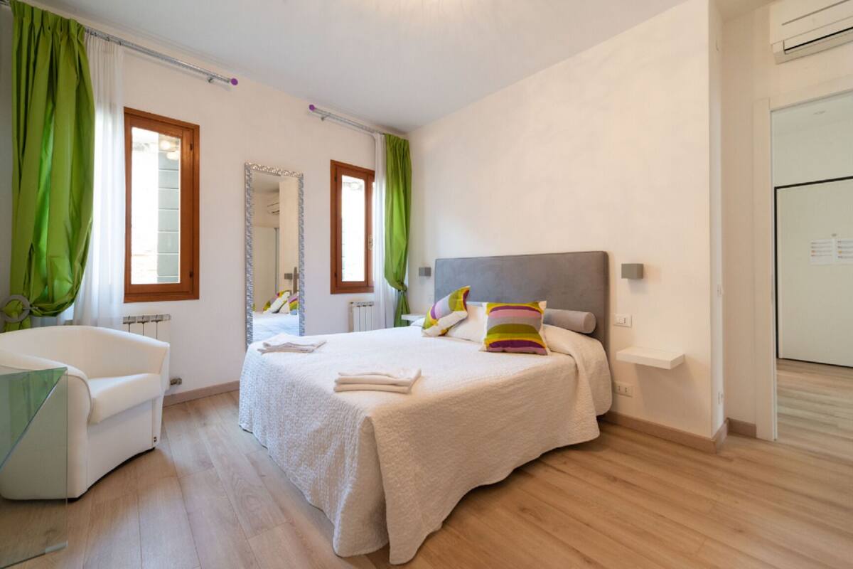 Un dormitorio con cama, una silla, un espejo y un radiador.