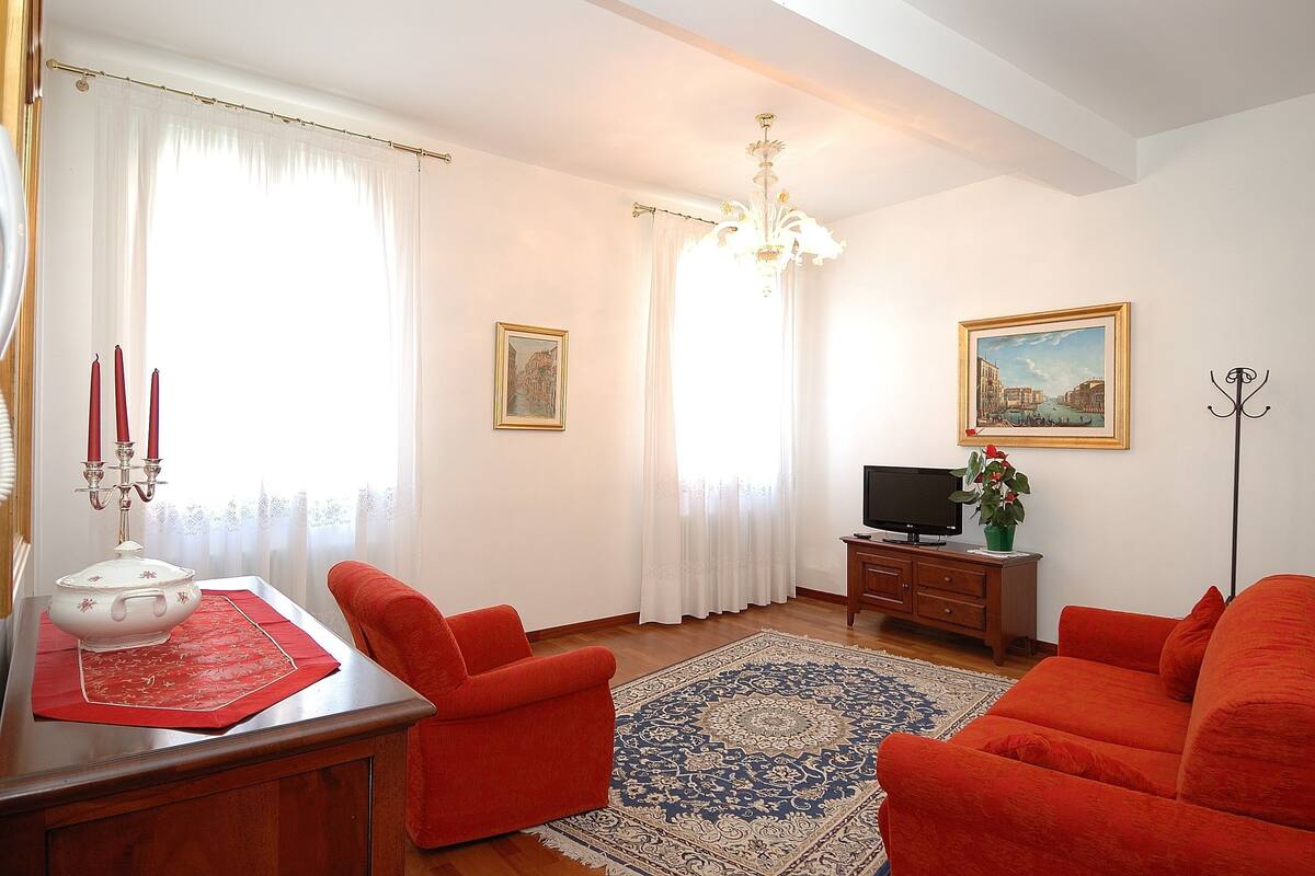 Una sala de estar con un sofá rojo, una mesa de centro de madera, un televisor y una araña.