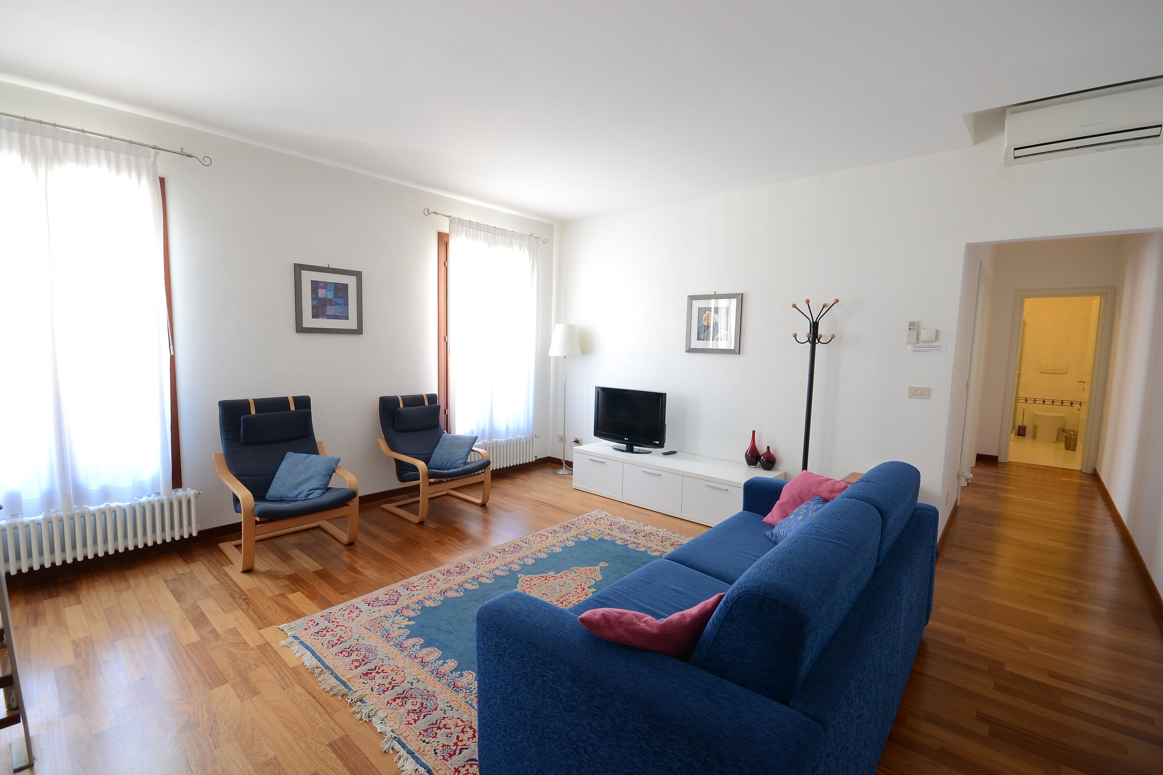 A living room with a blue sofa, two armchairs, a television, and a radiator.