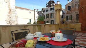 Una mesa en el balcón con una cesta de fruta, platos de galletas y tazas de té.