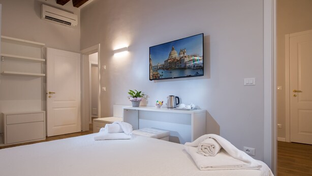 Habitación de hotel con cama, escritorio, silla, planta en maceta y cuadro de un paisaje urbano.