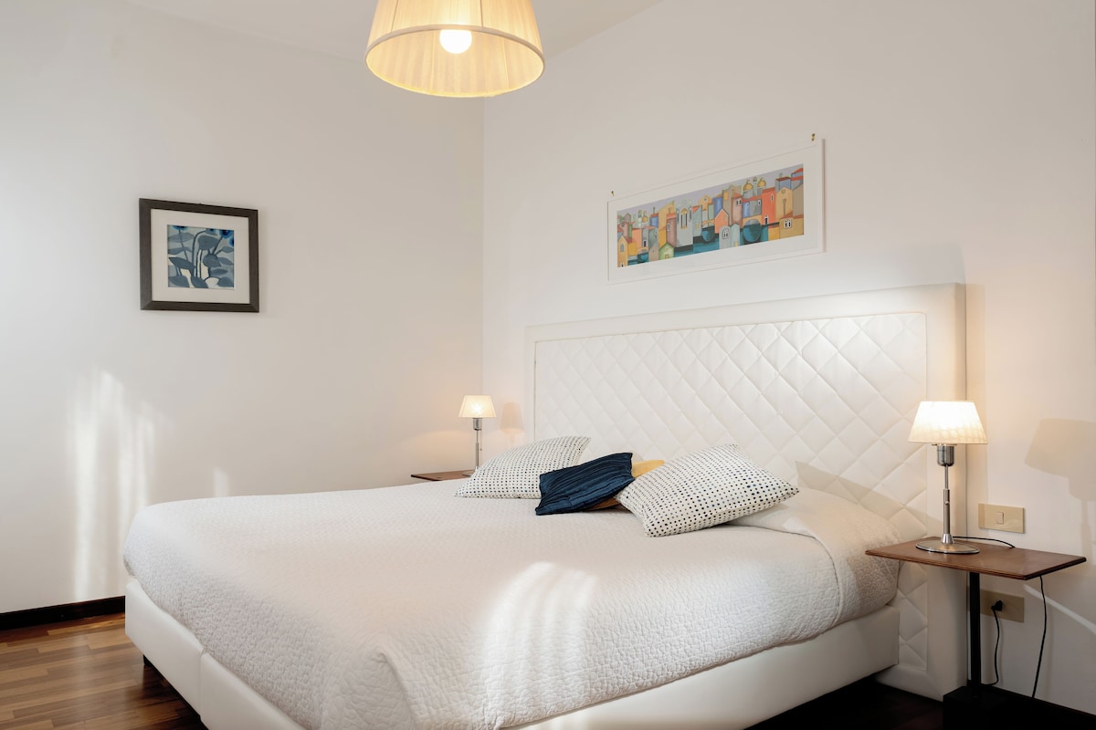 A neatly made bed with a quilted headboard, a bedside table with a lamp, and a framed picture on the wall.