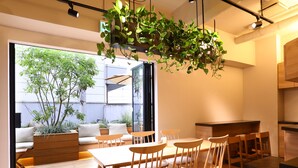 A modern interior with a wooden dining table and chairs, a kitchen area, and a large window overlooking a garden. - KOKO HOTEL Korakuen (Tokyo)