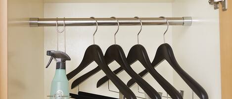 A closet with a metal rod holding black hangers and a teal spray bottle.