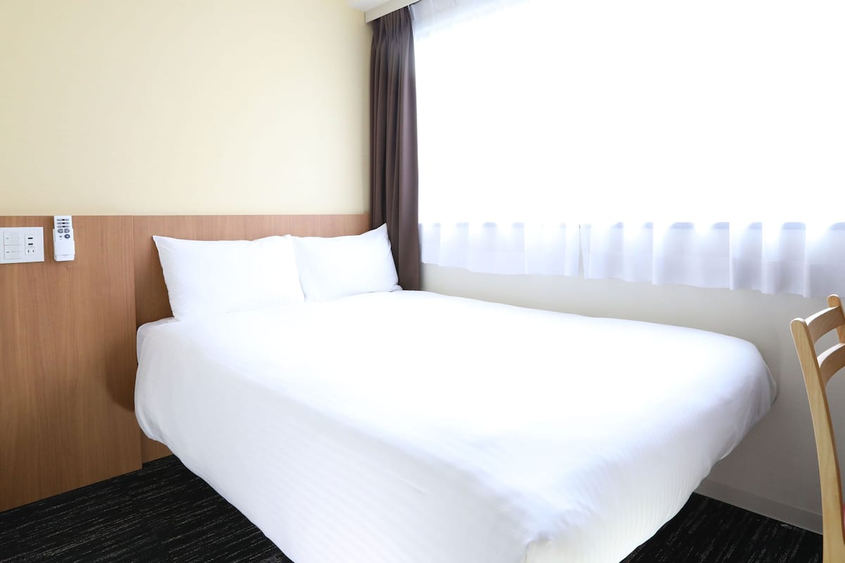 A hotel room with a large bed, a wooden headboard, a desk with a chair, and a window with curtains.