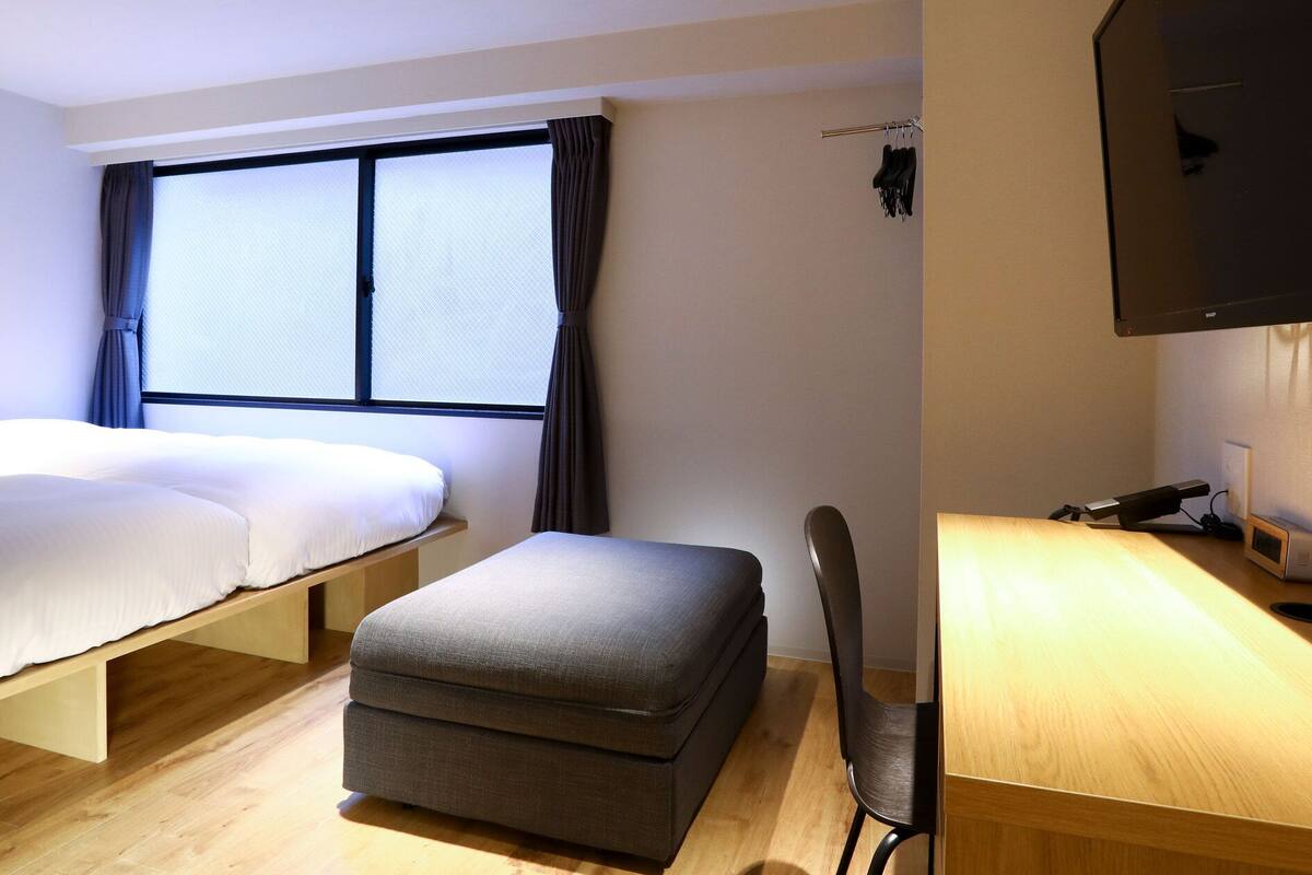 A hotel room with a bed, a small seating area, a desk with a lamp, and a TV mounted on the wall.