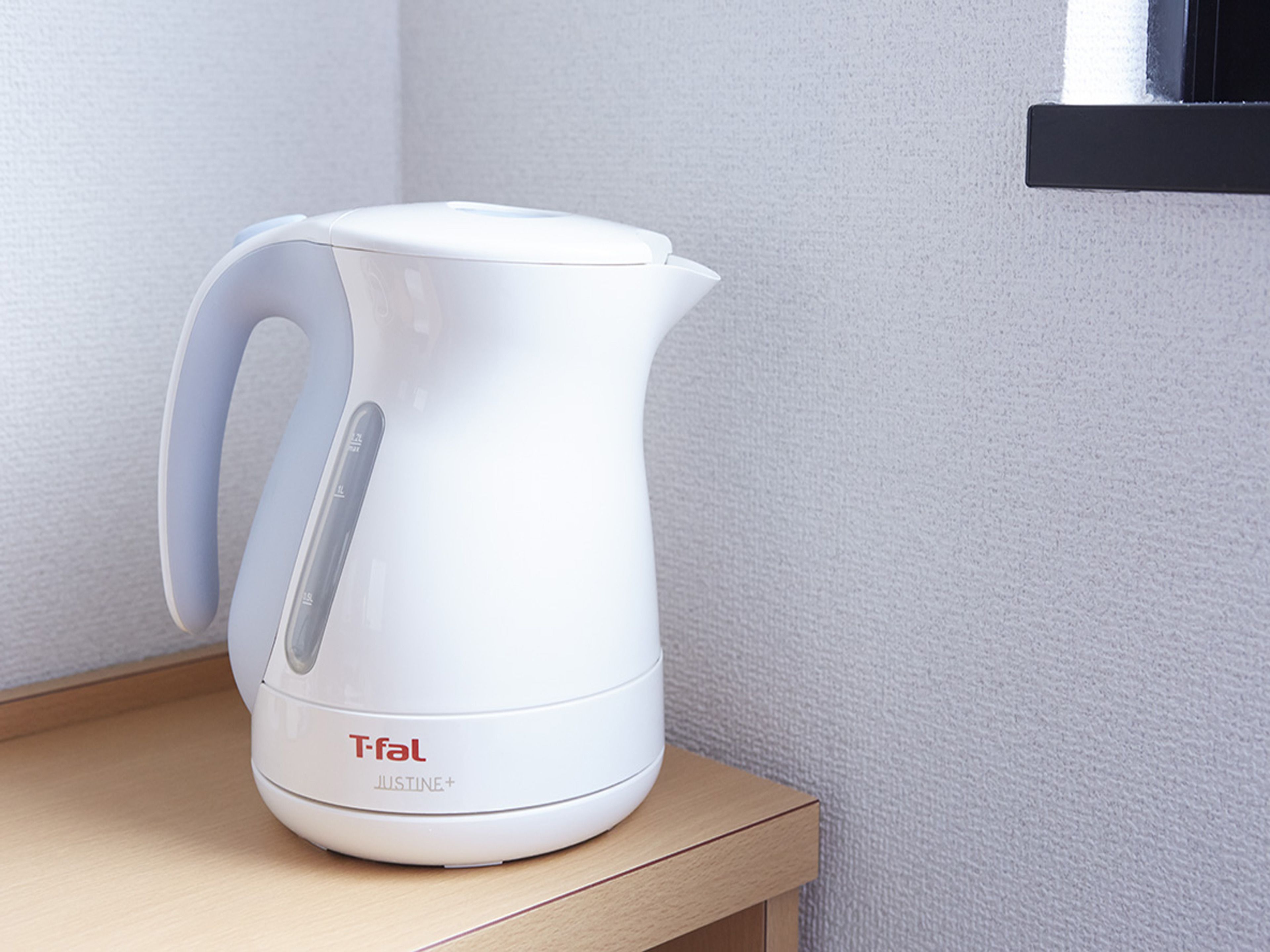 A white Tefal Justine+ electric kettle on a wooden surface against a textured wall.