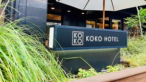 A sign for Koko Hotel with a large umbrella and surrounding greenery. - KOKO HOTEL Korakuen (Tokyo)