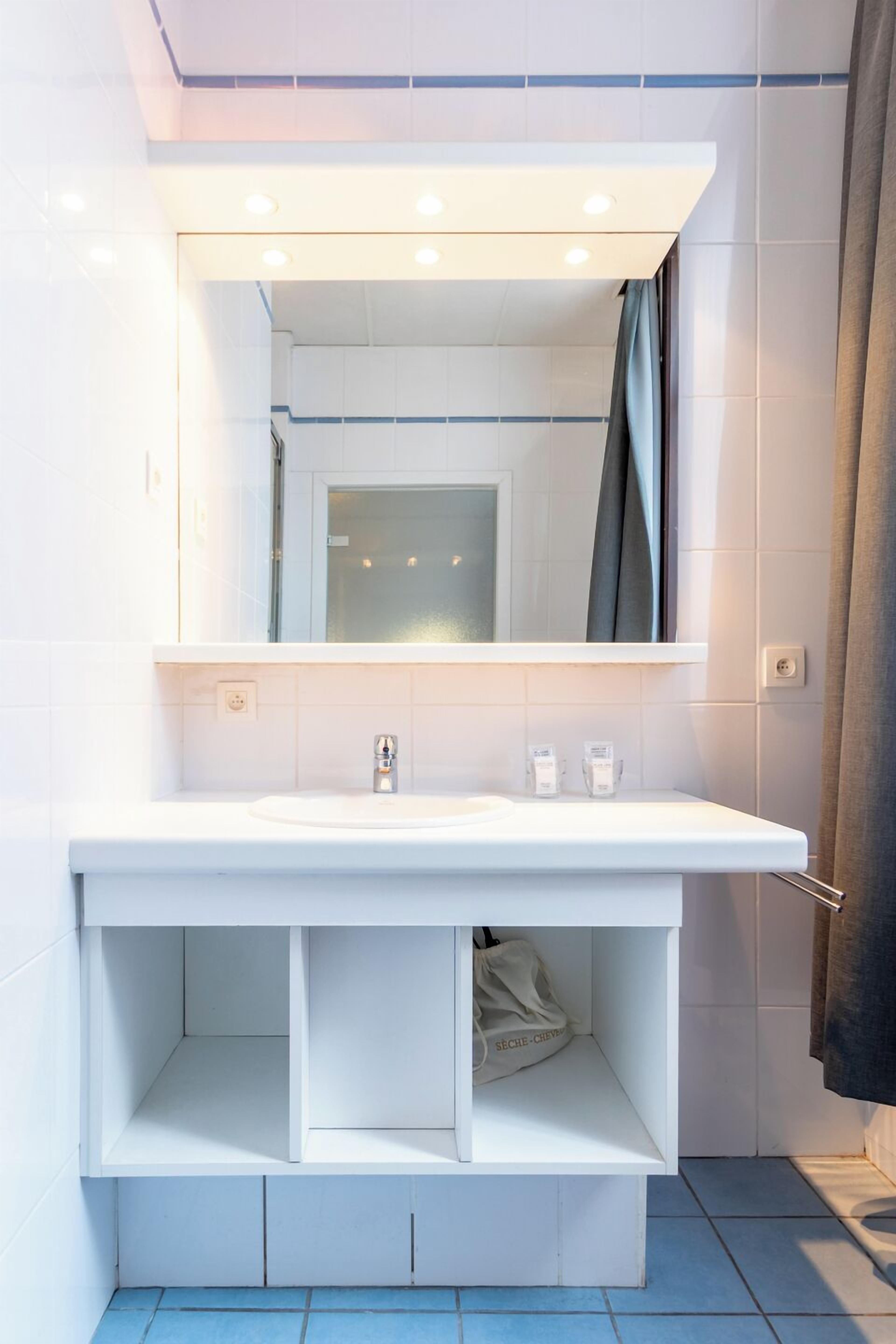 Un baño moderno con tocador blanco, un espejo y zona de ducha.