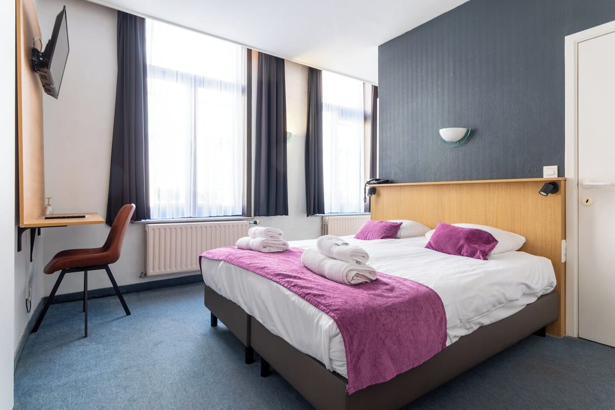 A modern hotel room with a bed, a desk, and a chair.